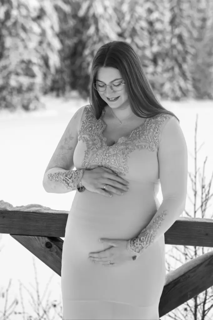 Babybauchshooting mit verschneitem Wald im Hintergrund